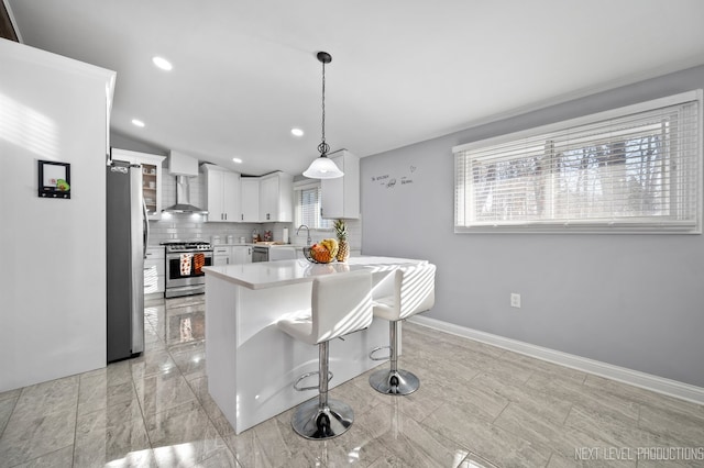 kitchen featuring pendant lighting, wall chimney range hood, decorative backsplash, white cabinetry, and stainless steel appliances