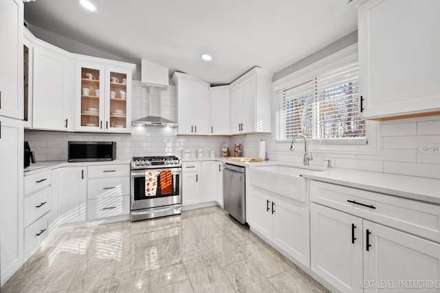 kitchen with sink, stainless steel appliances, wall chimney range hood, tasteful backsplash, and white cabinets