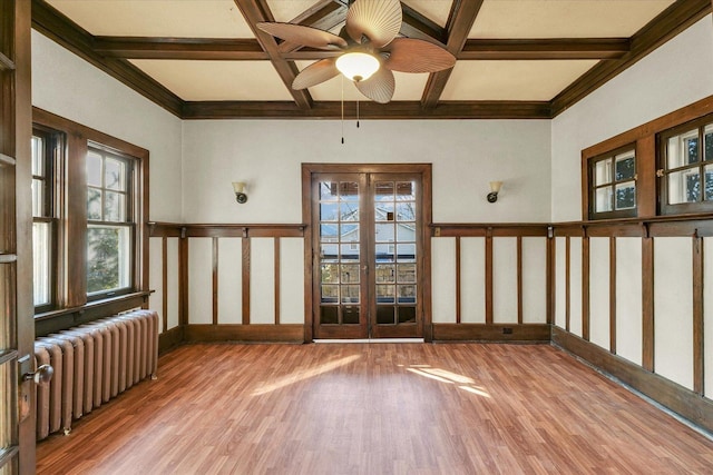 empty room featuring radiator heating unit, light hardwood / wood-style flooring, coffered ceiling, beam ceiling, and french doors