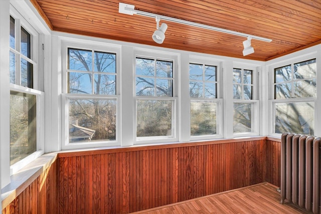 unfurnished sunroom featuring wood ceiling, track lighting, and radiator