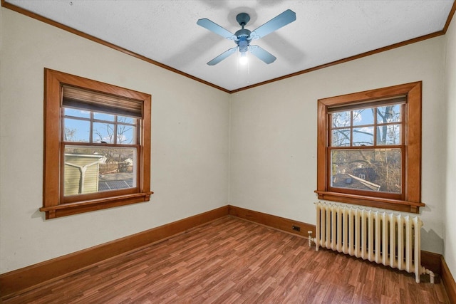 spare room featuring radiator, wood-type flooring, ornamental molding, and plenty of natural light