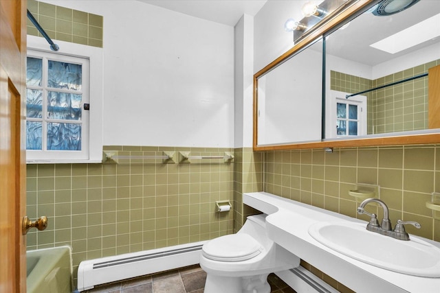 bathroom featuring toilet, sink, a skylight, tile walls, and a baseboard heating unit