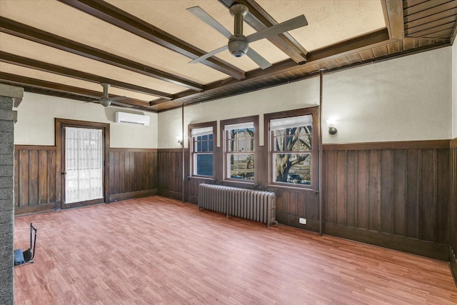 spare room with radiator, wooden walls, wood-type flooring, ceiling fan, and beam ceiling