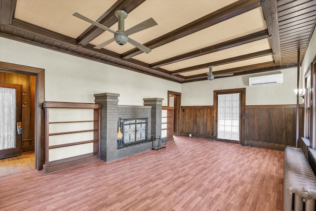 unfurnished living room with a wall mounted AC, a brick fireplace, radiator heating unit, hardwood / wood-style flooring, and beam ceiling