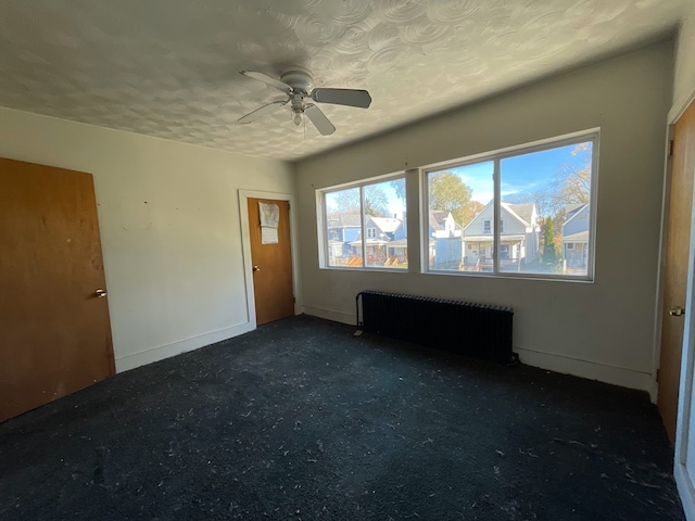 empty room with radiator heating unit, a textured ceiling, dark carpet, and ceiling fan