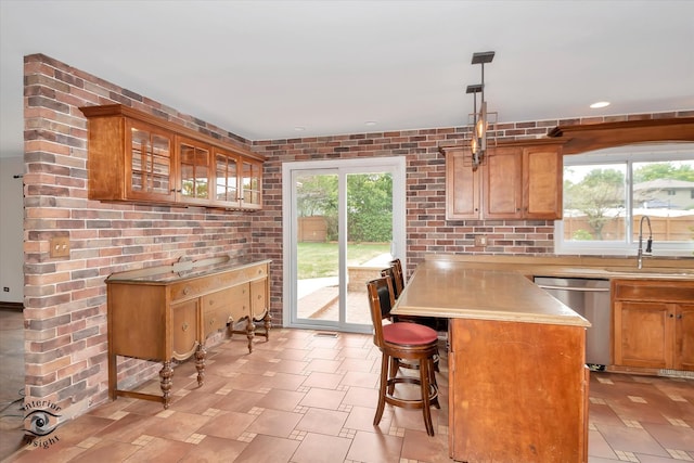 kitchen with a kitchen bar, stainless steel dishwasher, brick wall, sink, and pendant lighting