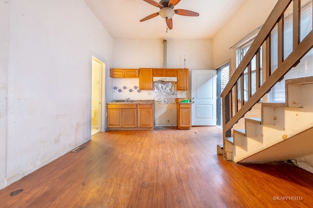 kitchen with backsplash, sink, light hardwood / wood-style flooring, ceiling fan, and a towering ceiling