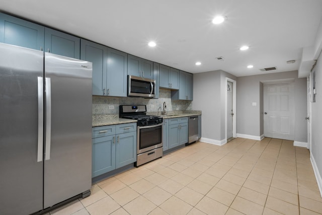 kitchen with backsplash, light stone counters, stainless steel appliances, sink, and blue cabinetry