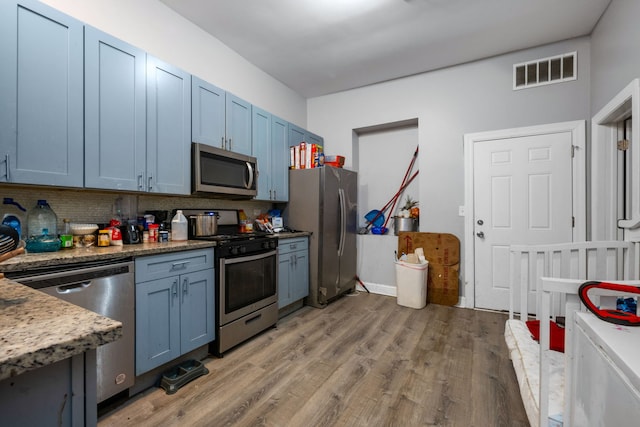 kitchen with appliances with stainless steel finishes, light wood-type flooring, blue cabinets, and backsplash