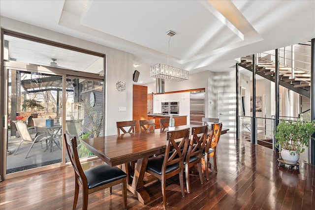 dining space featuring dark hardwood / wood-style flooring, a raised ceiling, and ceiling fan with notable chandelier