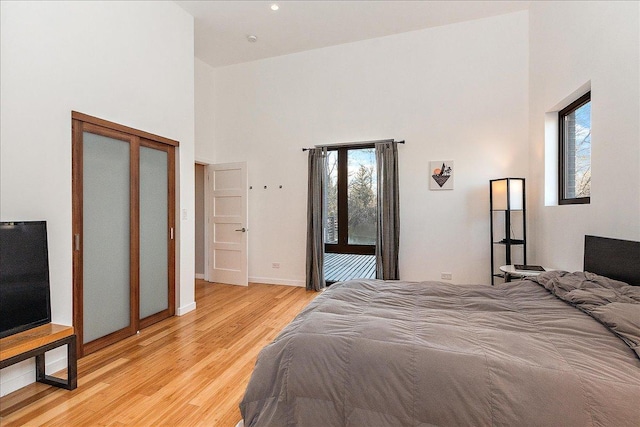 bedroom featuring light hardwood / wood-style floors, access to exterior, and a towering ceiling