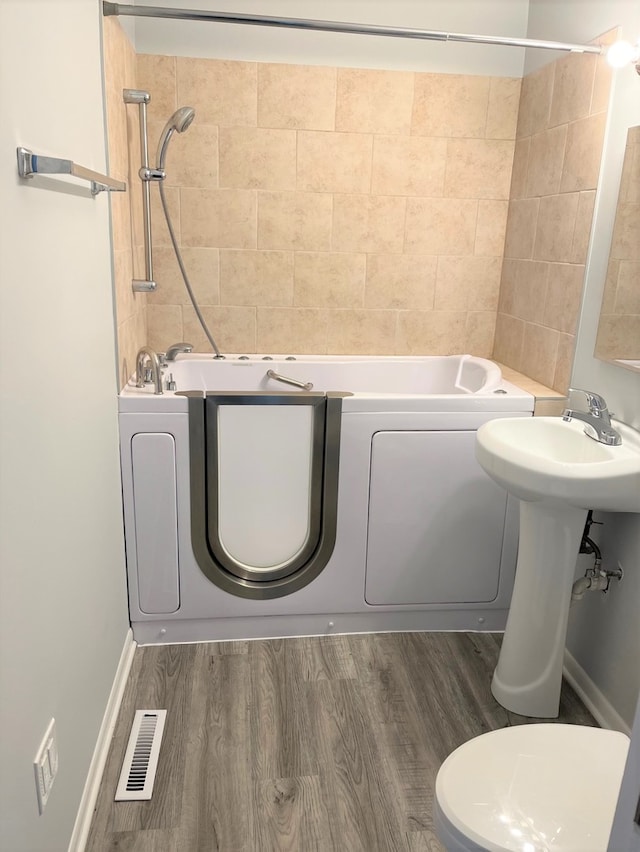 full bathroom featuring wood-type flooring, toilet, tiled shower / bath, and sink