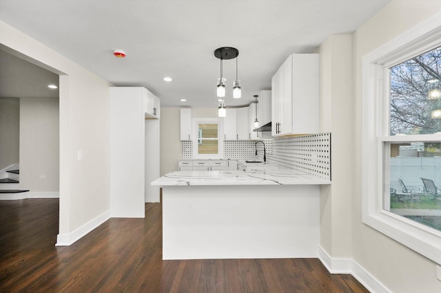 kitchen with backsplash, pendant lighting, kitchen peninsula, white cabinetry, and light stone counters