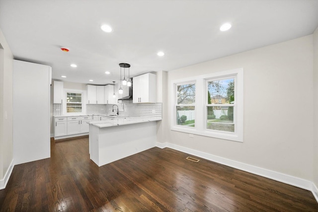 kitchen with backsplash, pendant lighting, kitchen peninsula, sink, and white cabinets