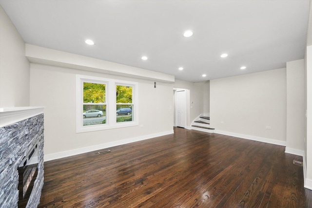 unfurnished living room with dark hardwood / wood-style flooring and a stone fireplace