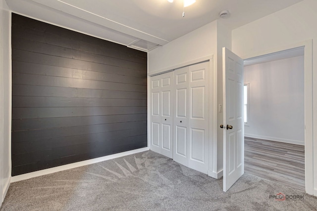 unfurnished bedroom featuring light carpet, a closet, and wood walls