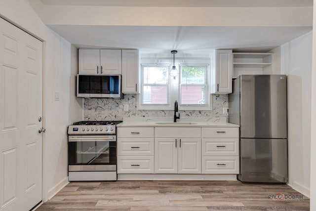 kitchen featuring pendant lighting, sink, light hardwood / wood-style flooring, decorative backsplash, and appliances with stainless steel finishes