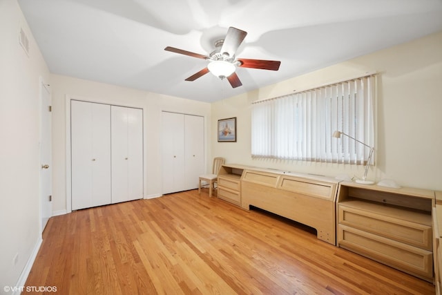 unfurnished bedroom featuring light wood-type flooring, ceiling fan, and multiple closets