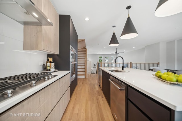 kitchen with wall chimney exhaust hood, stainless steel appliances, ceiling fan, sink, and hanging light fixtures