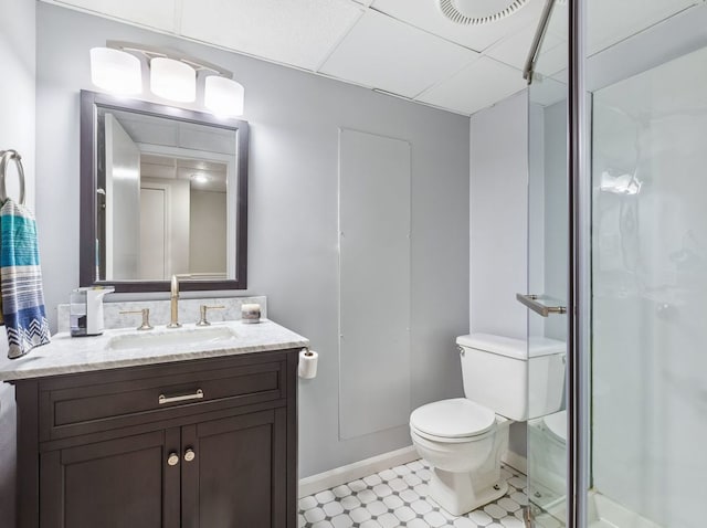 bathroom featuring a drop ceiling, tile patterned flooring, toilet, a shower with door, and vanity