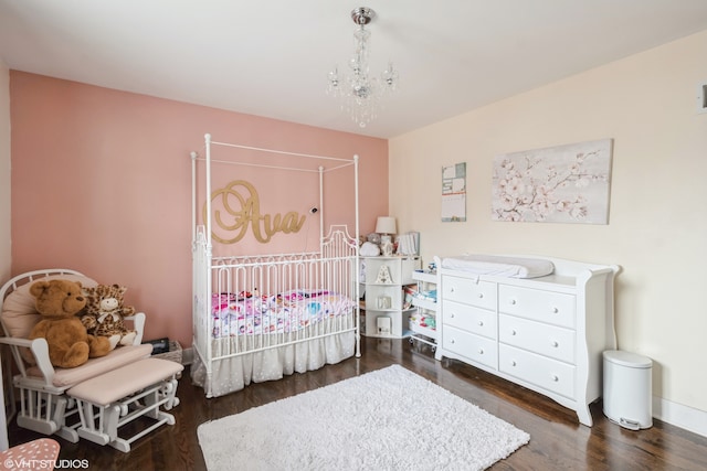 bedroom featuring a crib, dark hardwood / wood-style floors, and a chandelier