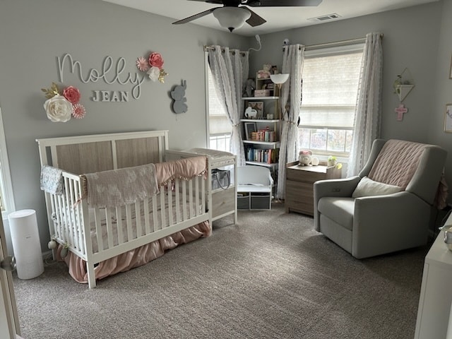 carpeted bedroom featuring ceiling fan and a crib