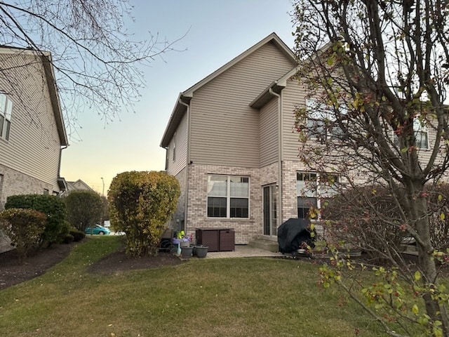 back house at dusk featuring a patio area and a yard