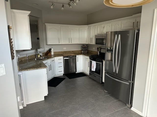 kitchen with appliances with stainless steel finishes, sink, dark tile patterned flooring, dark stone countertops, and white cabinets