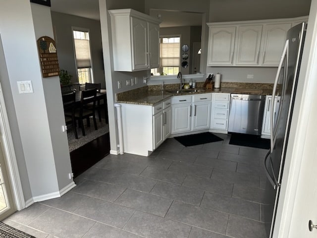 kitchen featuring appliances with stainless steel finishes, sink, dark stone countertops, white cabinets, and tile patterned flooring