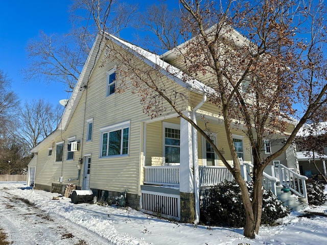 view of snow covered exterior featuring an AC wall unit and a porch