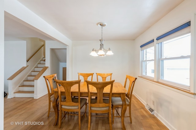 dining space with stairs, light wood-style flooring, a notable chandelier, and baseboards