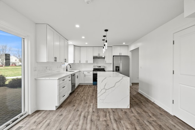 kitchen featuring light stone countertops, appliances with stainless steel finishes, a kitchen island, white cabinetry, and hanging light fixtures