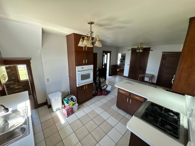 kitchen with white oven, light tile patterned floors, decorative light fixtures, and ceiling fan with notable chandelier