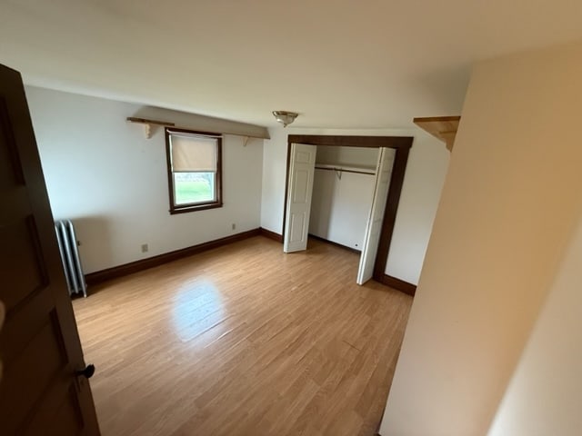 unfurnished bedroom featuring light wood-type flooring, radiator, and a closet