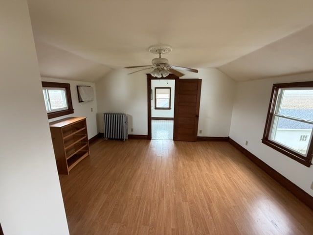 bonus room featuring vaulted ceiling, radiator heating unit, a wealth of natural light, and light hardwood / wood-style flooring