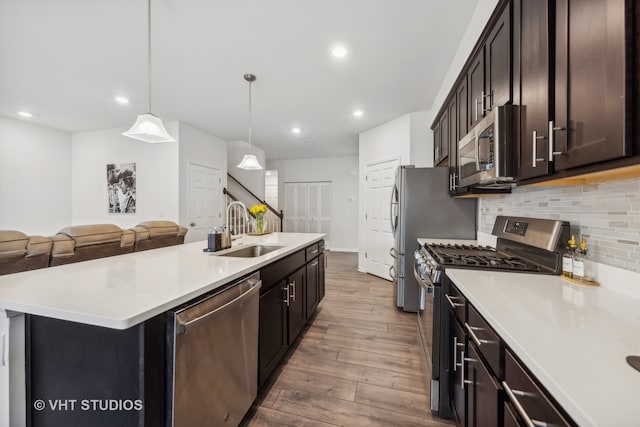 kitchen featuring hanging light fixtures, sink, an island with sink, appliances with stainless steel finishes, and wood-type flooring