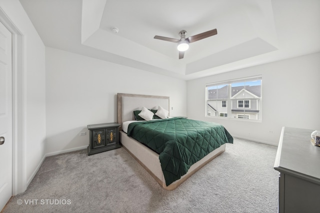 bedroom with a raised ceiling, ceiling fan, and light colored carpet