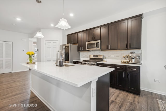 kitchen with dark brown cabinetry, stainless steel appliances, decorative light fixtures, a center island with sink, and hardwood / wood-style flooring