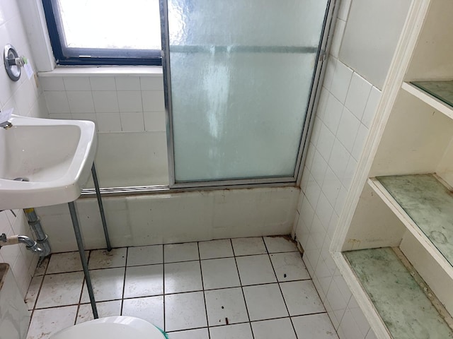 bathroom with tile walls, shower / bath combination with glass door, tile patterned floors, and toilet