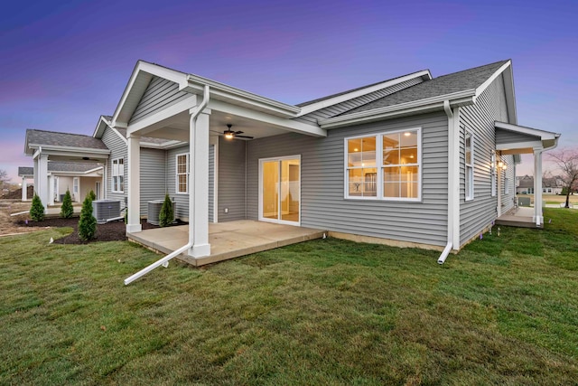 back house at dusk with a lawn, ceiling fan, a patio area, and central air condition unit