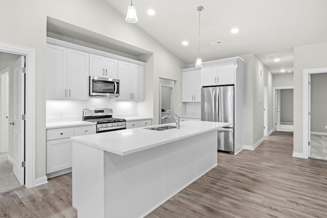 kitchen with white cabinetry, sink, hanging light fixtures, stainless steel appliances, and a center island with sink