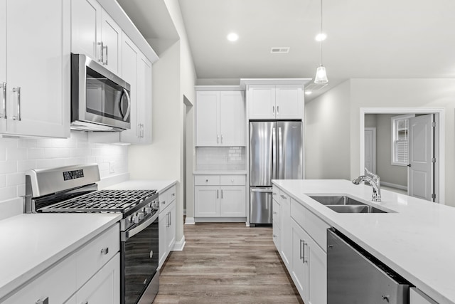 kitchen with sink, appliances with stainless steel finishes, pendant lighting, white cabinets, and light wood-type flooring