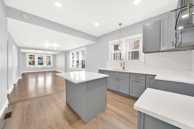 kitchen with gray cabinetry, sink, pendant lighting, light hardwood / wood-style flooring, and a center island