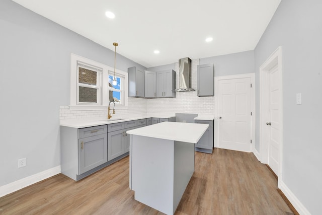 kitchen with a center island, sink, wall chimney range hood, decorative light fixtures, and gray cabinets