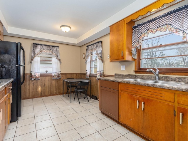 kitchen featuring plenty of natural light, black refrigerator, sink, and wooden walls