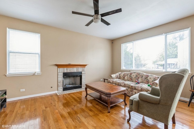 living room featuring ceiling fan, light hardwood / wood-style floors, and a brick fireplace