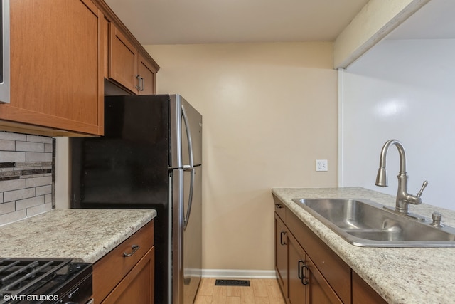 kitchen with stainless steel fridge, backsplash, black range oven, sink, and light hardwood / wood-style flooring