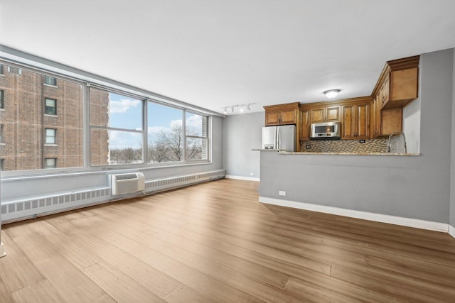 unfurnished living room featuring an AC wall unit, rail lighting, and light hardwood / wood-style flooring