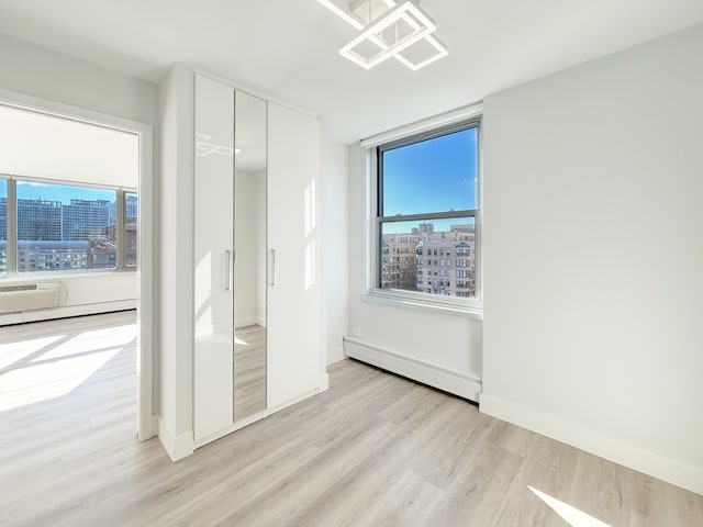 unfurnished bedroom featuring baseboard heating, a closet, and light wood-type flooring