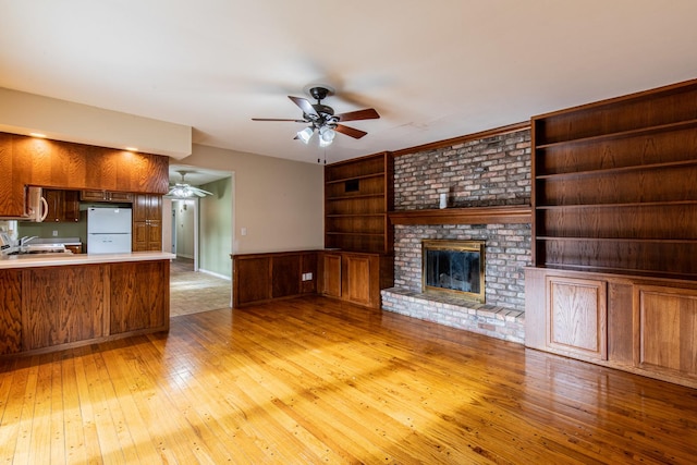 unfurnished living room featuring a fireplace, ceiling fan, built in features, and light hardwood / wood-style flooring